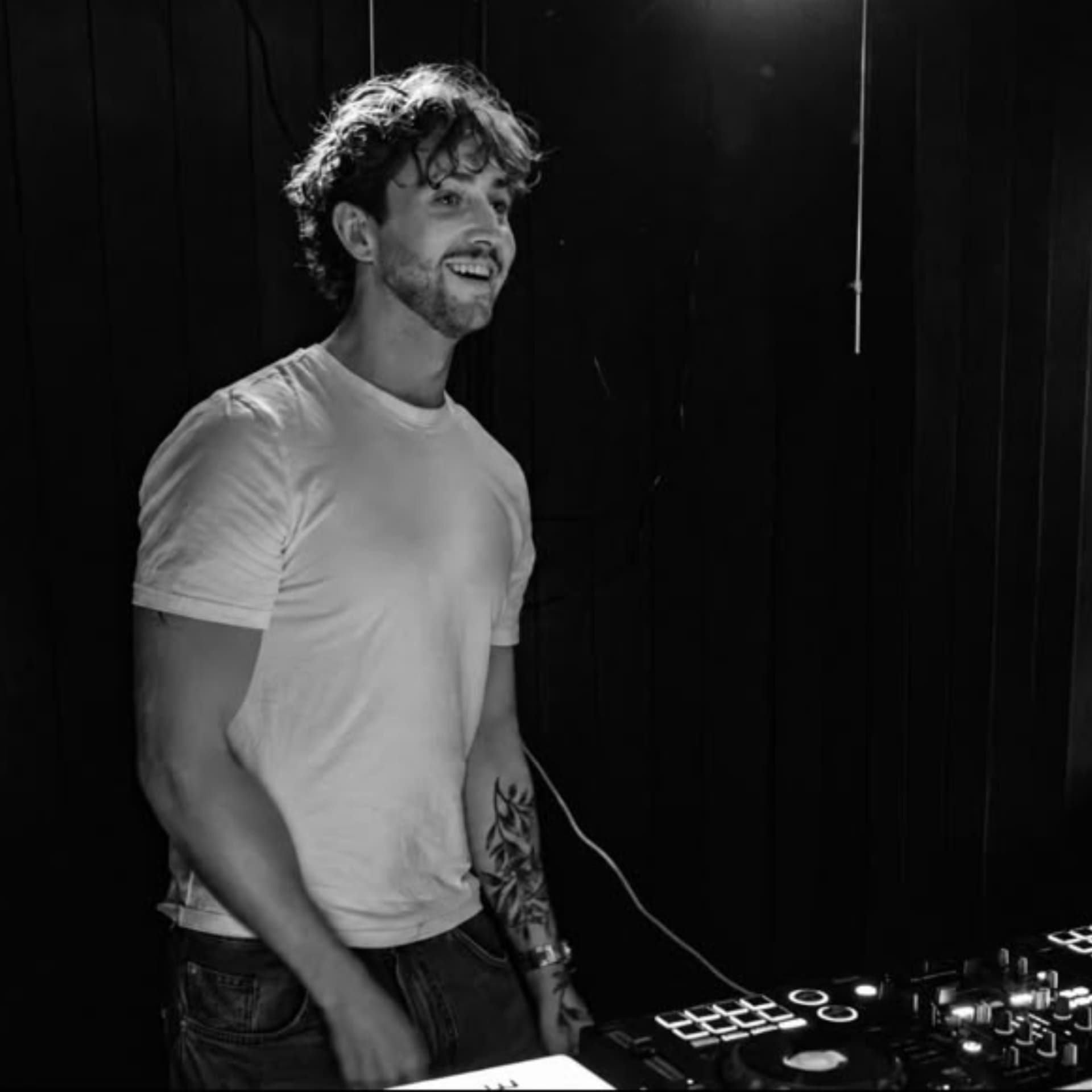 Romario smiling behind the decks during his set at Duecourse Old Town Takeover in Hastings, black and white